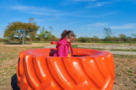 Foto de Niña jugando en una rueda de tractor de colores brillantes en una feria de granja en Halloween - Imagen libre de derechos