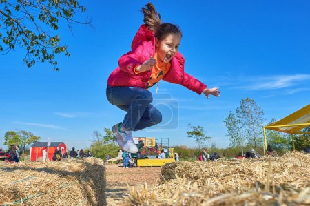 Foto de Chica bonita saltando sobre las pilas de heno en una feria de granja en Halloween - Imagen libre de derechos