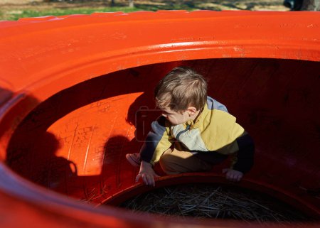 Foto de Lindo niño jugando dentro y sobre una rueda de tractor colorido en la feria de granja en Halloween - Imagen libre de derechos