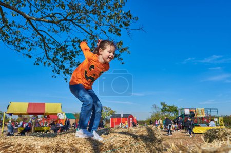 Foto de Chica bonita saltando sobre las pilas de heno en una feria de granja en Halloween - Imagen libre de derechos