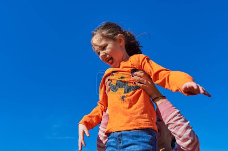 Foto de Bonita chica siendo sostenida en el aire por mamá contra un cielo azul - Imagen libre de derechos