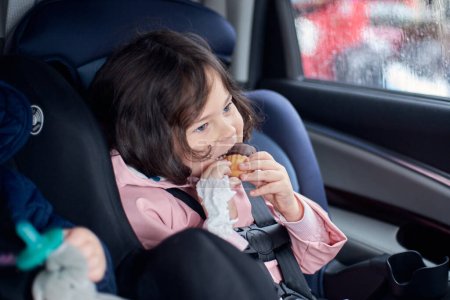 Photo for Siblings in car seats having snacks in the back seat of a car on a rainy day - Royalty Free Image