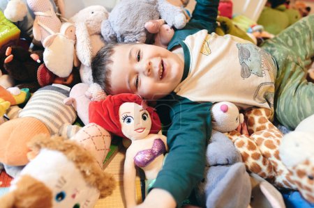 Photo for Cute young boy playing among a mountain of soft plush toys - Royalty Free Image