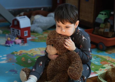 pensive baby boy hugging a toy bear in the kids room at nap time