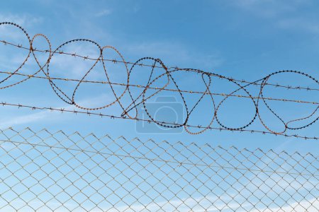 A fence with barbed wire against a blue sky. Restricted area.