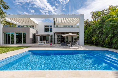 Photo for Backyard of beautiful, elegant and modern house in miami, with pool, short grass, trees, wall of palms, sun loungers with umbrellas, balcony, chairs and table, summer kitchen - Royalty Free Image