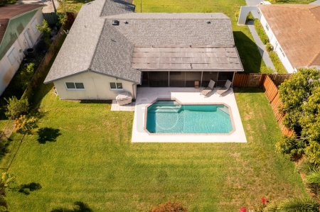 Téléchargez les photos : Vue aérienne du drone à la cour arrière de la maison, piscine, patio couvert avec fenêtres avec moustiquaire, herbe courte, cuisine d'été, chaises longues, clôture en bois, arbres et buissons, bardeaux d'asphalte - en image libre de droit