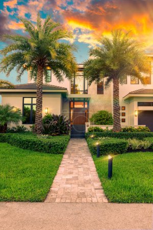 Foto de Elegante casa moderna, vista de la entrada con camino, camino de entrada, árboles grandes, plantas tropicales, acera - Imagen libre de derechos
