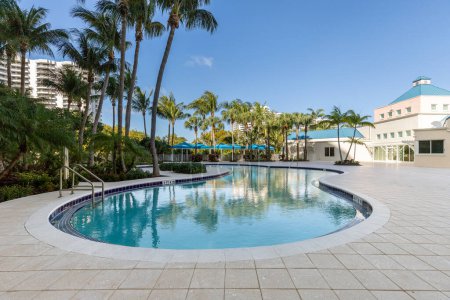 Foto de Área de piscina en edificio con gazebos, suelo de cemento, palmeras de plantas tropicales, edificios en el fondo y cielo azul - Imagen libre de derechos