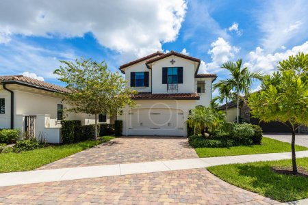 Colonial house facade in Pembroke Pines suburb of Miami, cobblestone driveway, sidewalk, tropical plants, red roof tiles, palm trees, blue sky