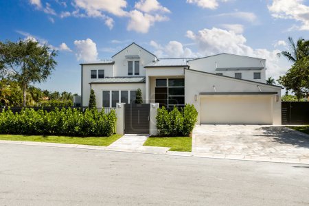 Photo for Front view of a modern stylish white house with walkway to front door, garage, short grass, trees, palms, privet fringe, sidewalk, blue sky - Royalty Free Image