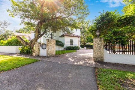 Photo for Elegant facade of a colonial-style house in the Riviera neighborhood, in Coral Gables, white walls with red tiles, stone details, short grass, trees, driveway and path to the front door - Royalty Free Image