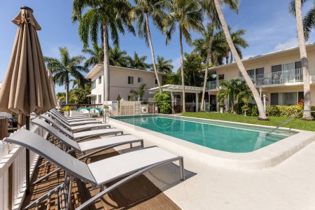 Point of view of pool, with parked boats, sun loungers with umbrellas, white metal fence fence, palms, balls, blue sky, in the Nurmi Isles neighborhood, Fort Lauderdale, Florida