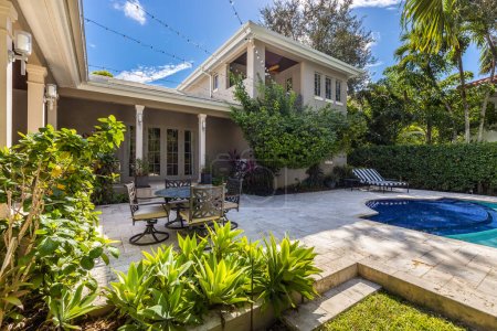 Photo for Backyard of elegant and luxurious mansion, with palms and lots of plants around, beautiful pool, covered patio, outdoor furniture, shortgrass, basketball court and blue sky with clouds - Royalty Free Image