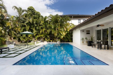 Florida, USA. September: Backyard of a modern house with swimming pool, artificial grass, stone floor, trees, chairs and an umbrella.