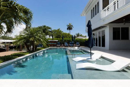 Florida, Estados Unidos. Septiembre: Patio trasero de una casa moderna con piscina, césped artificial, suelo de piedra, árboles, sillas y un paraguas.