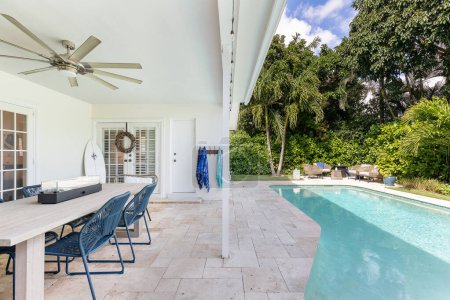 Florida, USA. September: Backyard of a modern house with swimming pool, artificial grass, stone floor, trees, chairs and an umbrella.