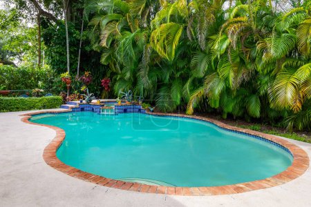 Florida, USA. September: Backyard of a modern house with swimming pool, artificial grass, stone floor, trees, chairs and and umbrella.