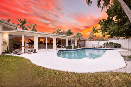 Florida, USA. September: Backyard of a modern house with swimming pool, artificial grass, stone path, trees, chairs and an umbrella.