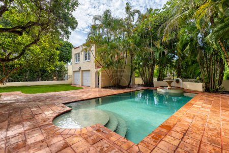 Florida, USA. January: Backyard of a modern house with swimming pool, artificial grass, stone path, trees, chairs and an umbrella.
