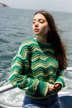 Young woman in knitted sweater standing on ferry boat with sea at background in Turkey 