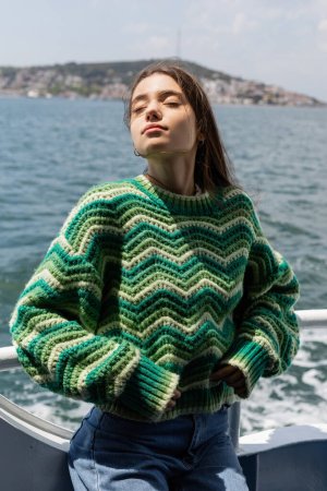 Young woman in knitted sweater standing on yacht with sea and Princess islands at background in Turkey 