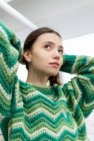 Young woman in knitted sweater touching hair and looking away on yacht 