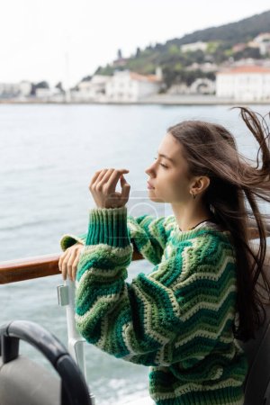 Téléchargez les photos : Vue latérale de la jeune femme en pull debout près de la rampe sur le yacht en Turquie - en image libre de droit