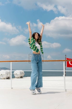 Positive junge Frau hebt Hände und springt auf Jacht in der Türkei 