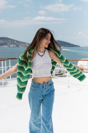 Überglückliche Frau mit Pullover steht bei Kreuzfahrt in der Türkei auf Jacht 
