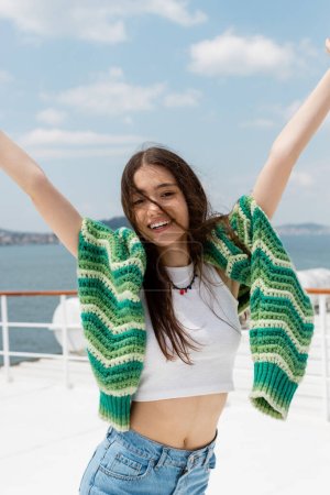 Fröhliche junge Frau in Top und Pullover blickt während einer Kreuzfahrt auf einem Fährschiff in der Türkei in die Kamera 