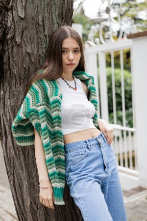 Photo for Brunette woman in top and knitted sweater standing near tree on street in Istanbul - Royalty Free Image