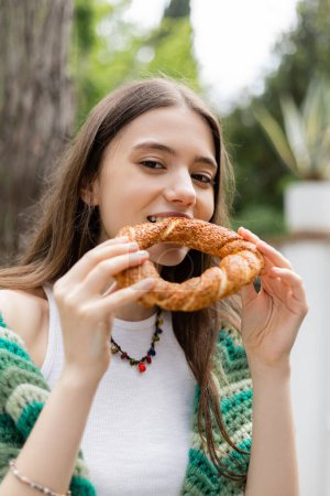 Retrato de una joven comiendo pan simit y mirando a la cámara en Estambul