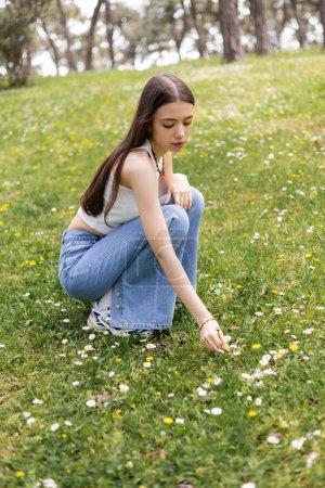 Brunette woman in top looking at daisy flowers on lawn in summer 