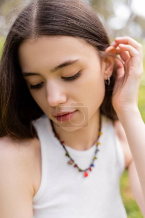 Photo for Portrait of young woman in top touching brunette hair outdoors - Royalty Free Image
