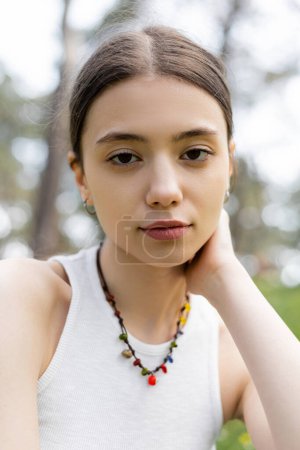 Photo for Portrait of young brunette woman in top and necklace looking at camera outdoors - Royalty Free Image