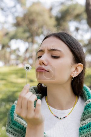 Foto de Mujer joven enfocada mirando la flor de la margarita en el borroso parque de verano - Imagen libre de derechos