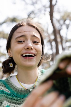 Fröhliche Frau mit Gänseblümchen im Haar blickt in die Kamera und lacht im Park 