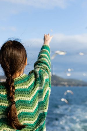 Back view of young woman in sweater outstretching hand and feeding blurred birds in Turkey 