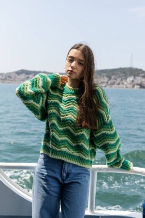 Portrait of brunette woman in knitted sweater looking at camera during cruise on ferry boat in Turkey 