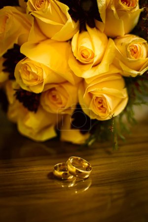 Wedding rings on the table with bouquet in the background