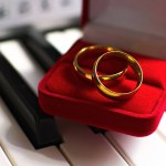 wedding rings on top of piano or keyboard keys. The image conveys an idea of an engagement or marriage request.