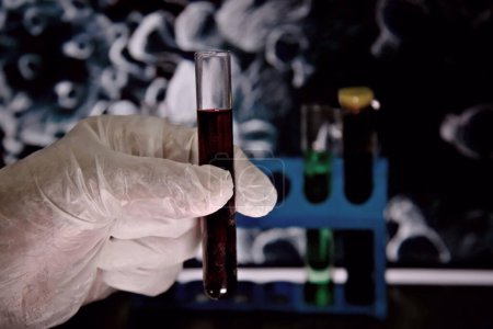 La mano con guantes blancos sostiene un tubo de ensayo con líquido. Medio ambiente de laboratorio.
