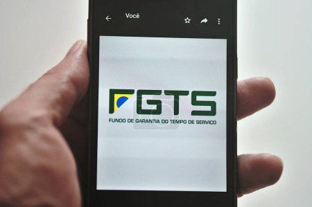 Hand holding cell phone with FGTS (Service Time Guarantee Fund) logo. Brazilian financial fund created by companies in the worker's name to help them after dismissal.