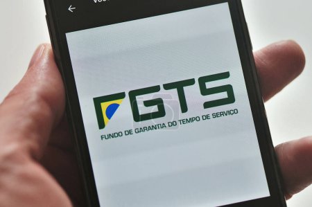 Hand holding cell phone with FGTS (Service Time Guarantee Fund) logo. Brazilian financial fund created by companies in the worker's name to help them after dismissal.