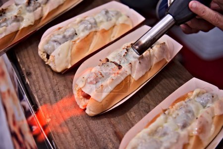 sausage sandwich with slices of cheese on top being flambed on a counter. Street food