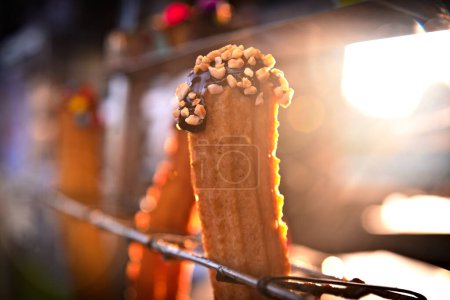 churro stuffed with chocolate and peanuts. In the background there is a beautiful light as a counter light. Street food