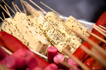 Curd cheese skewers seasoned with herbs and sausages on a counter. Street food