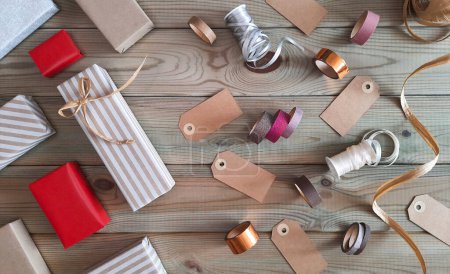 Photo for Preparing for the winter holidays: shopping, sales, gift wrapping. Flat lay. Decorating gift boxes for Christmas, New Year, Valentine's Day. Top view colored boxes, ribbons, tags on wooden background. - Royalty Free Image