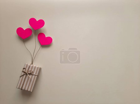 Photo for Selection, purchase, packaging, delivery of gift for holiday, mother's day. Top view. Copy space. Gift in a striped box on balloons in form of hearts on light background. Flat lay. Space for text - Royalty Free Image